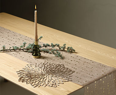 Zlatna stolna prostirka na drvenom stolu sa svijećom