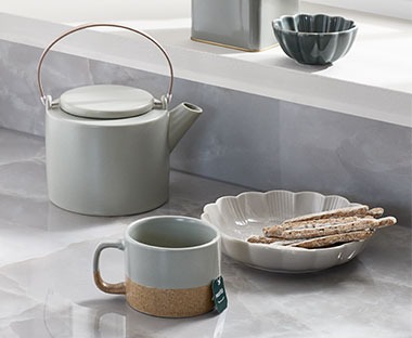Čajnik, šalica i zdjelica u sivoj boji na stolu