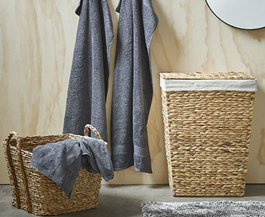 Pleteni koš za rublje u kupaonici kraj sivih ručnika