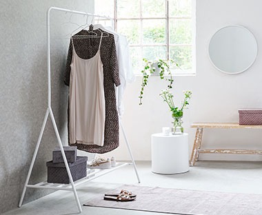 Bijeli stalak za odjeću s kutijama za pohranu, natur klupa, ogledalo i dekoracija
