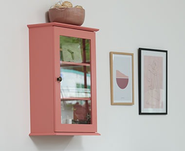 Zidni ormarić roze boje sa staklenim vratima na zidu