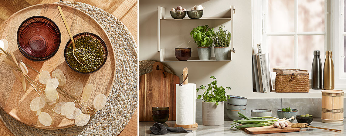 Staklene zdjele na pletenom podmetaču i kamene šalice sa svježim začinskim biljem na zidnoj polici u kuhinji