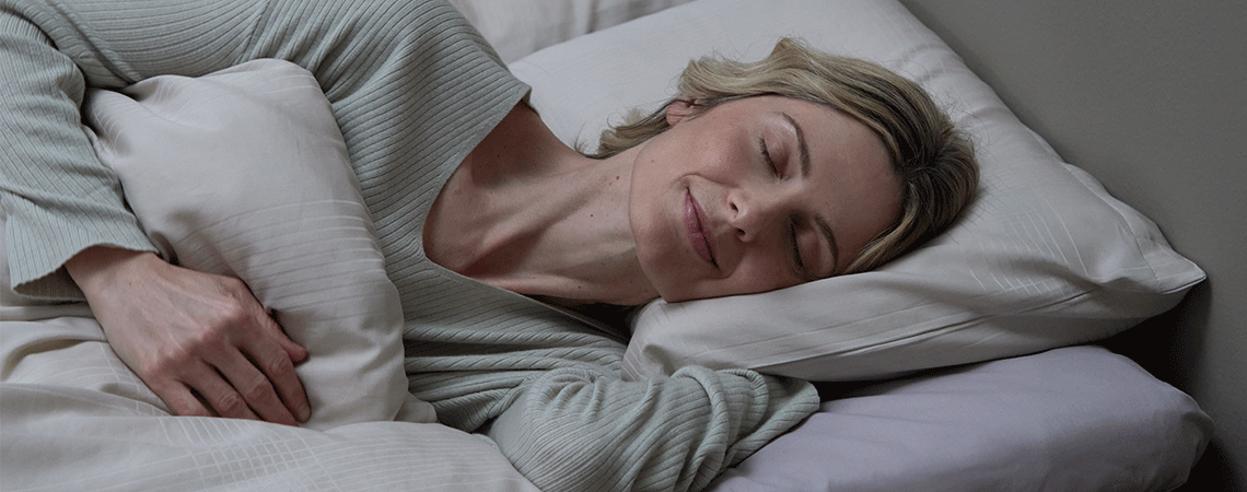 Žena spava na boku u krevetu s bijelim jastukom i poplunom