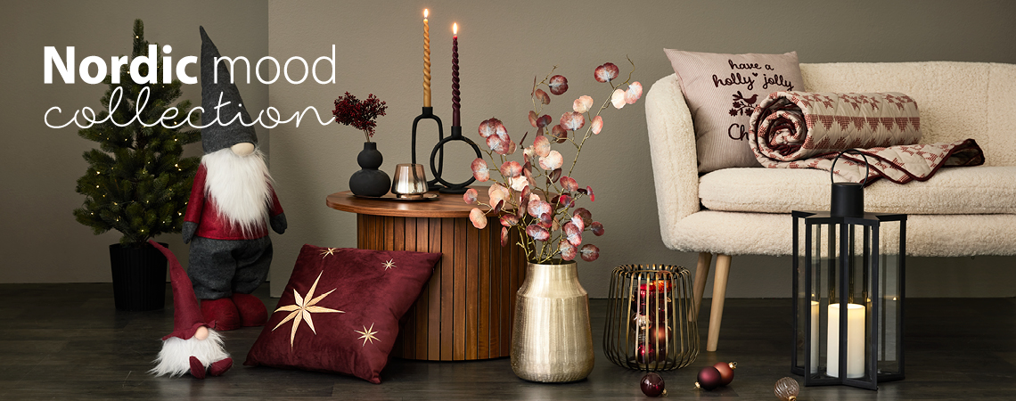 Božićni patuljci, jastučići, zlatna vaza s umjetnim cvijećem, zlatni svijećnjak i crni fenjer ispred bijele sofe