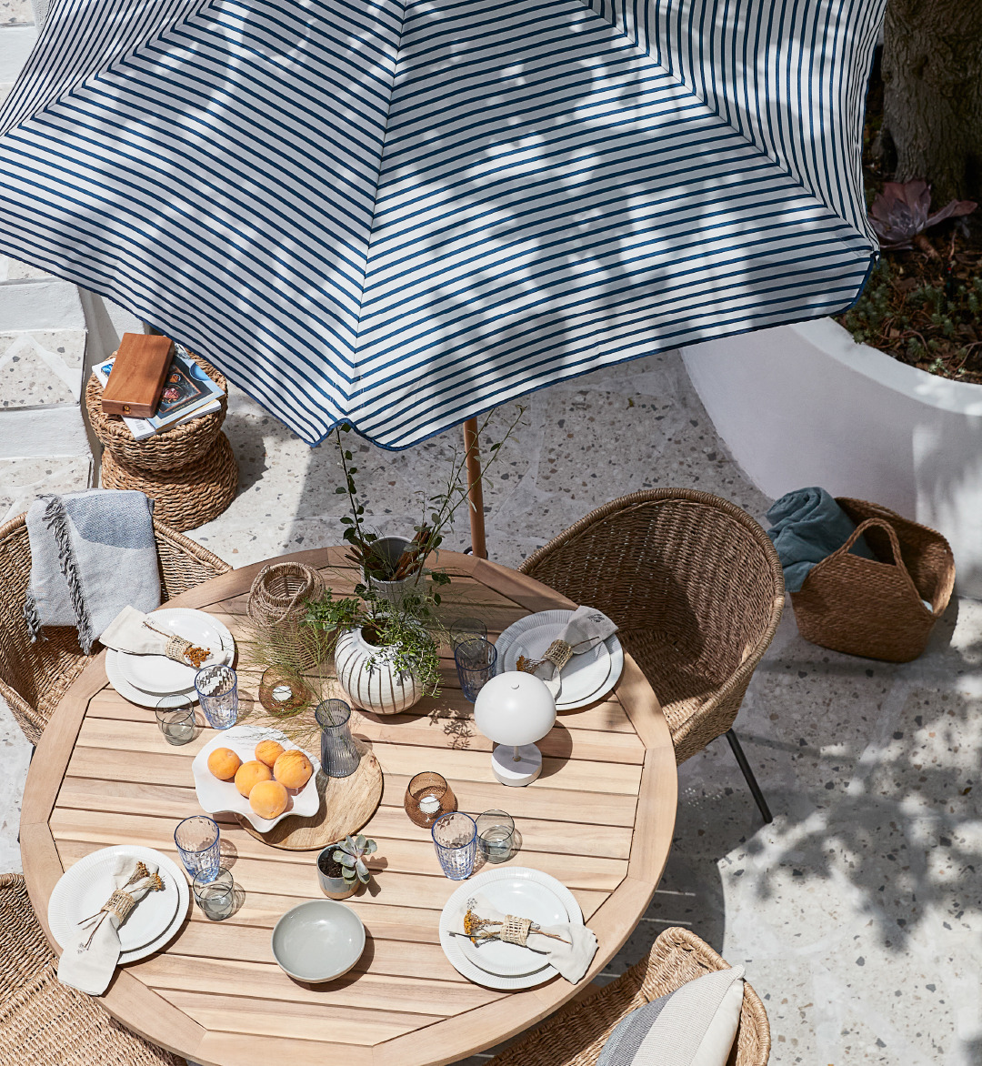 Postavljeni vrtni stol i stolice ispod prugastog suncobrana na terasi