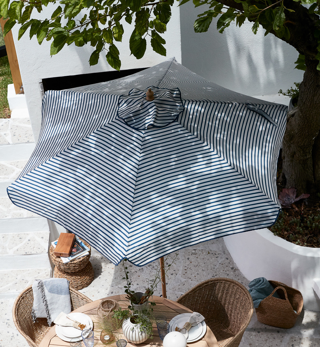 Prugasti bijelo-plavi suncobran na terasi iznad vrtnog stola i stolica