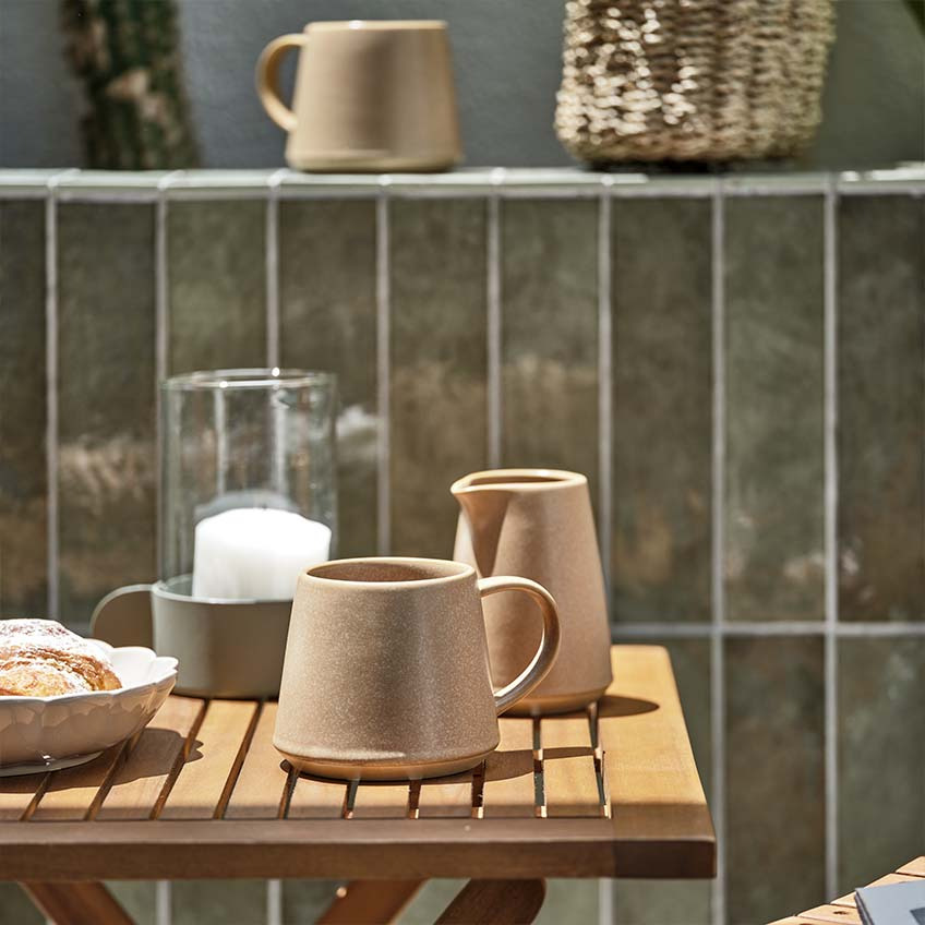 Šalica za kavu i staklenka za mlijeko na malom drvenom vrtnom stolu 