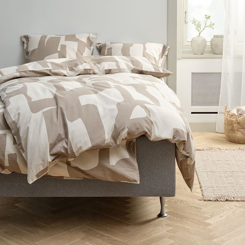 Set posteljine u tamnoj boji pijeska i bež s grafičkim dizajnom na krevetu u spavaćoj sobi