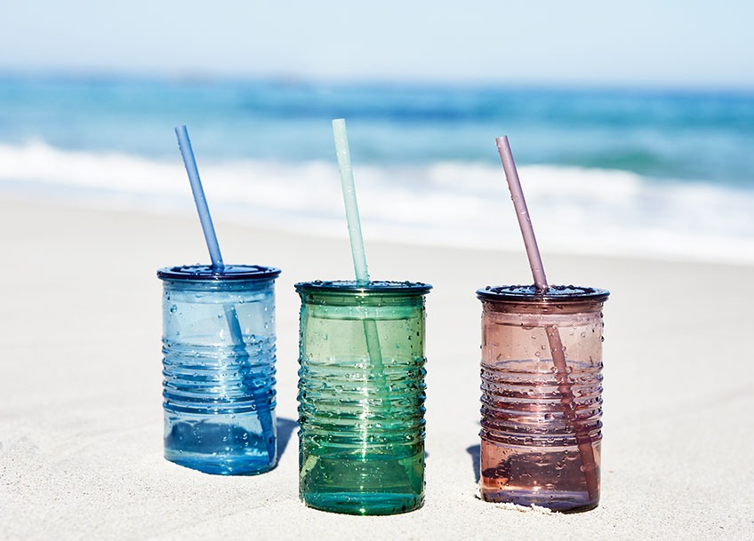 Tri čaše sa slamkom u raznim bojama u pijesku na plaži