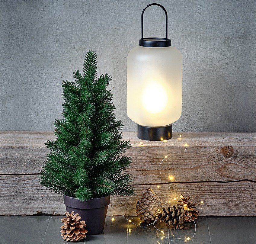 Umjetno božićno drvce, stakleni fenjer matiranog izgleda i lampice oko njih