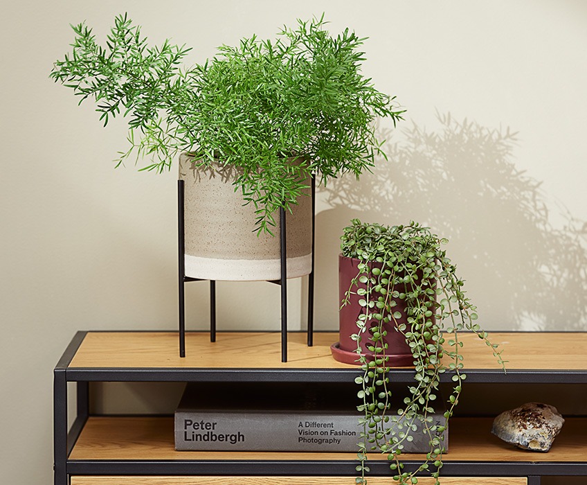Umjetne biljke na modernom stalku za TV, jedna biljka stoli uspravno, a druga visi 