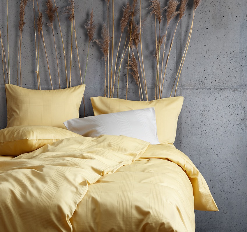 Žuta posteljina i lagani uzroci inspiriraju vas da se isključite, opustite i prepustite se Žuta posteljina napravljena od 51% recikliranog poliestera i 49% pamučnog satena u spavaćoj sobi betonskih zidova