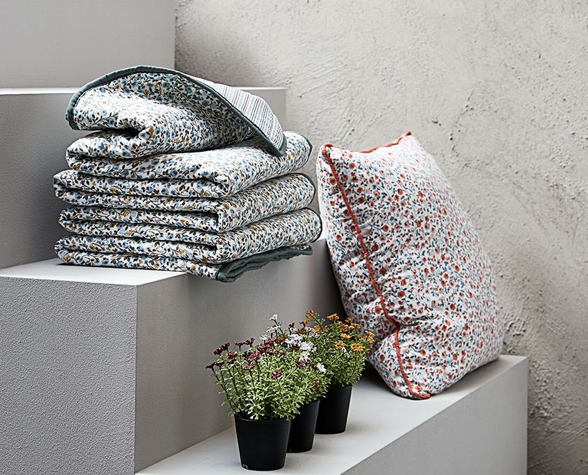 Stepienice s cvjetnim uzorkom na dekama i jastucima i tri umjetne biljke