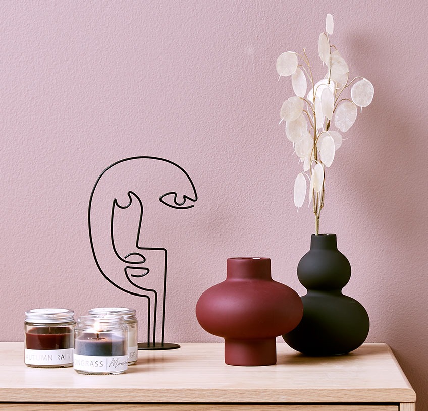 Cvjetna vaza na stolu sa skulpturom i tri mirisne svijeće