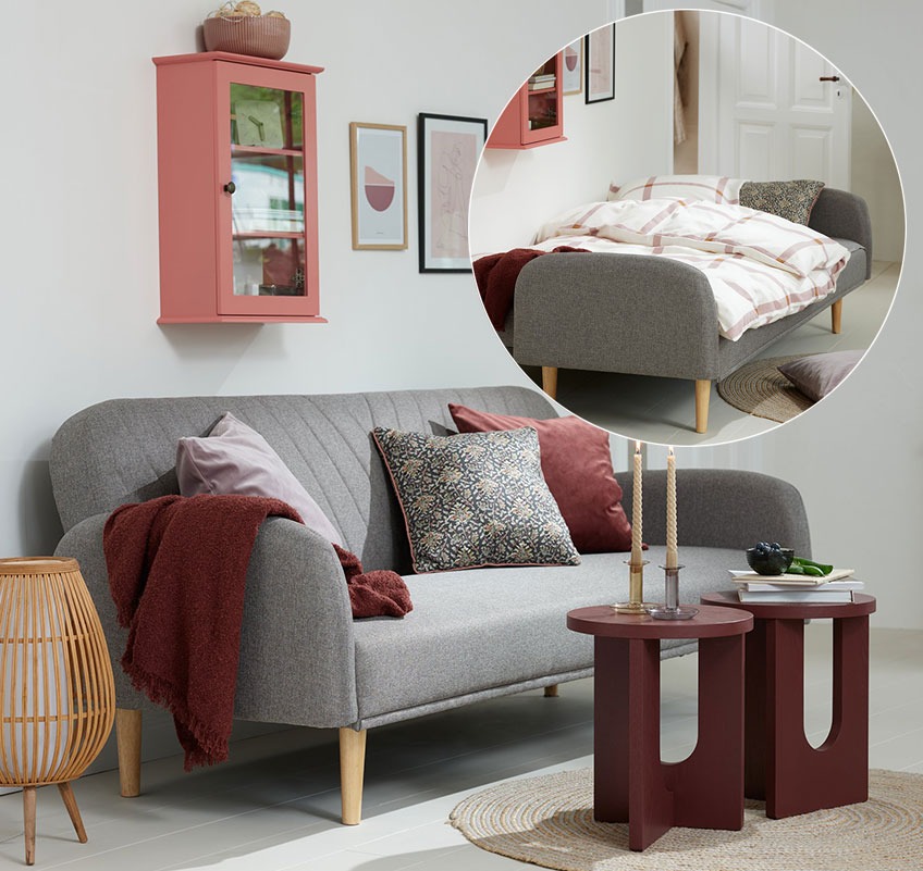 Zidni ormarić u rozoj boji, sivi kauč na razvlačenje i bordo stolići