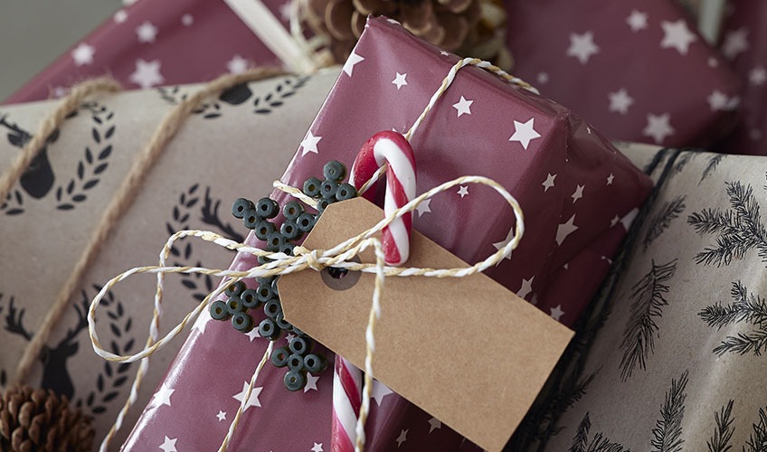 Božićni dar zamotan u papir i ukrašen bombonima i perlama