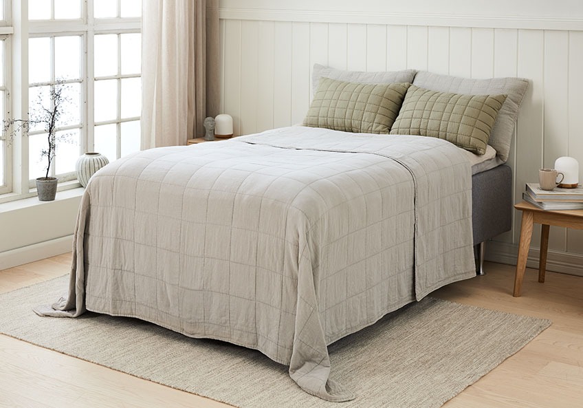 Krevet s štepanom dekom i odgovarajućim jastucima za leđa u svijetloj spavaćoj sobi