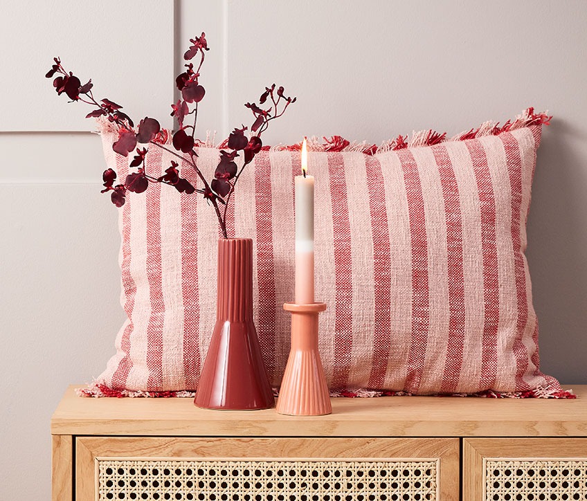 Prugasti jastuk iza crvene vaze i svijećnjaka s prugastom svijećom