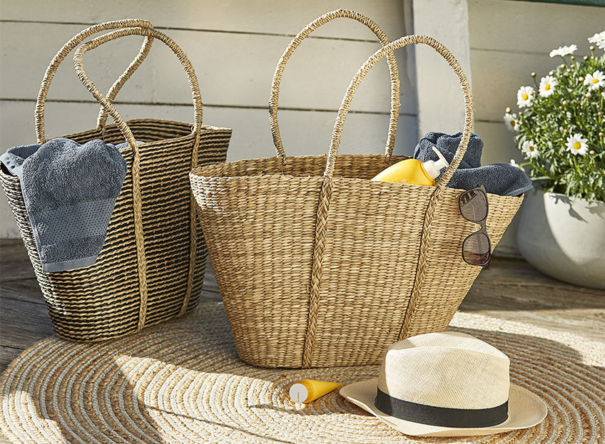 Two wicker beach bags with sunscreen and towels  