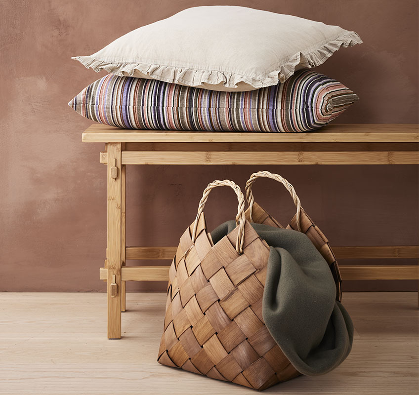 Dekorativni jastuci na drvenoj klupi i košara s dekom