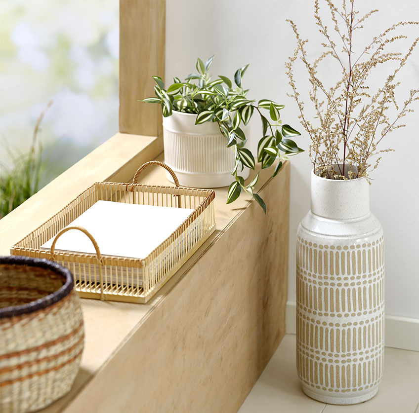 Visoka vaza pokraj prozorske klupice s posudom od bambusa i bijelom vazom s umjetnom biljkom