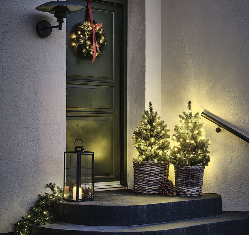 Dva svjetleća drvca ispred ulaznih vrata i božićni vijenac s crvenom mašnom