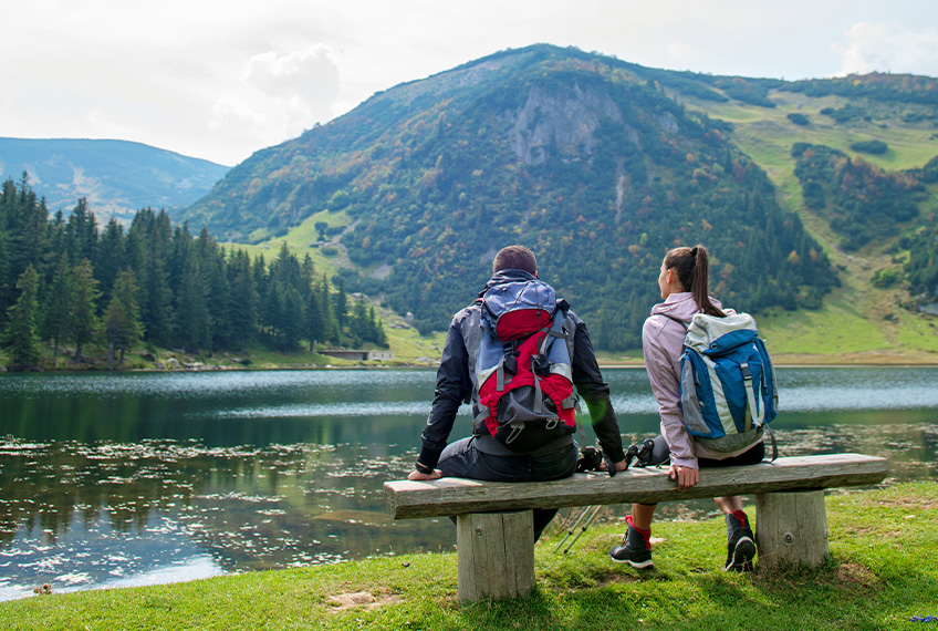 Muškarac i žena sjede na klupi i gledaju u planine i jezero