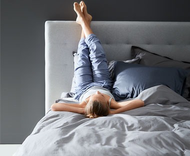 Žena se odmara na krevetu s nogama oslonjenima na zid